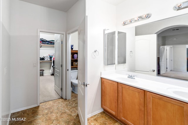 bathroom with baseboards, double vanity, toilet, a walk in closet, and a sink