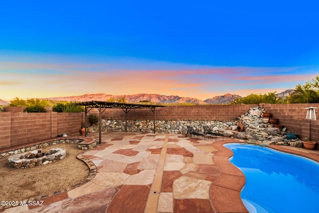 view of swimming pool featuring a mountain view, a fenced backyard, a fire pit, and a patio area