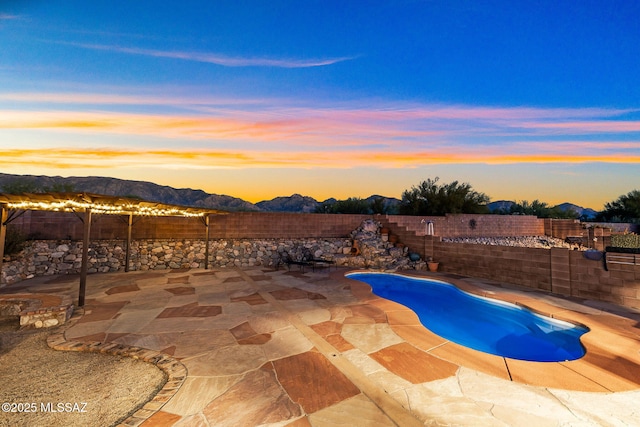 pool at dusk with a patio area, a mountain view, a fenced backyard, and a fenced in pool