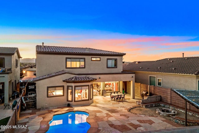 back of property at dusk with a fenced backyard, a tile roof, a patio, stucco siding, and a fenced in pool