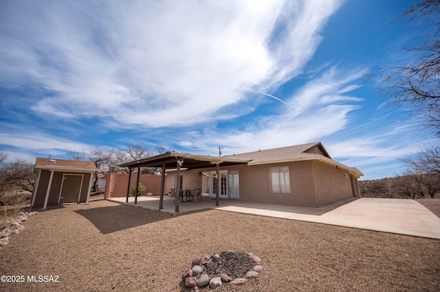 back of house featuring stucco siding, an outdoor structure, driveway, a storage unit, and a patio