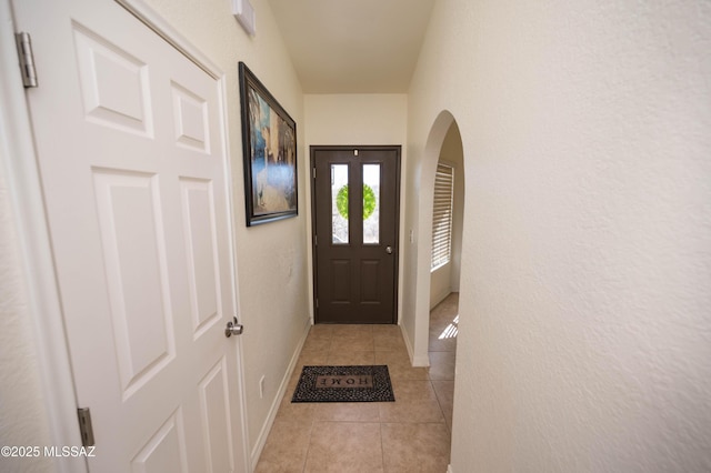 doorway to outside with light tile patterned floors, baseboards, and arched walkways