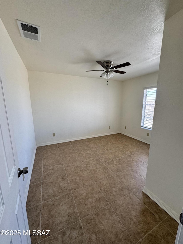 unfurnished room featuring visible vents, dark tile patterned floors, a textured ceiling, baseboards, and ceiling fan