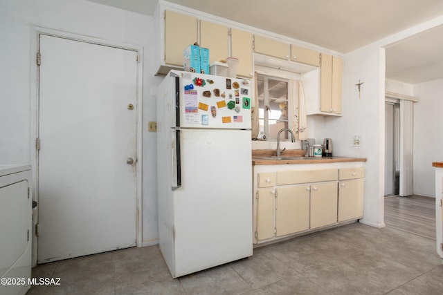 kitchen with freestanding refrigerator, washer / clothes dryer, a sink, light countertops, and cream cabinets