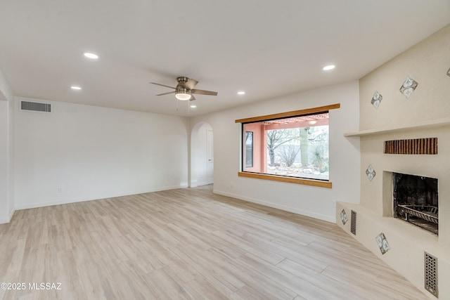 3053 W Lobo Rd, Tucson, AZ 85742 - unfurnished living room featuring visible vents, a fireplace with raised hearth, a ceiling fan, arched walkways, and light wood-style floors