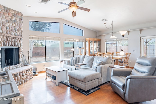 living room with a stone fireplace, vaulted ceiling, visible vents, ceiling fan, and wood finished floors