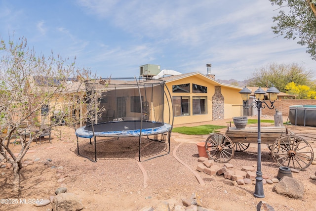 rear view of house featuring a trampoline, stucco siding, and fence
