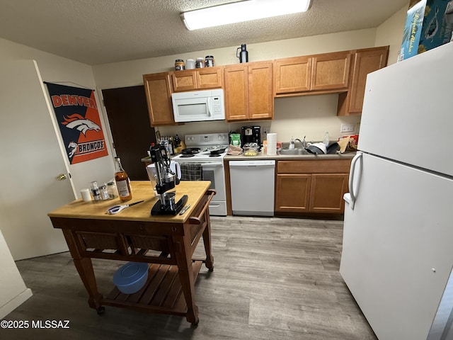 kitchen featuring a sink, white appliances, light wood-type flooring, and a textured ceiling