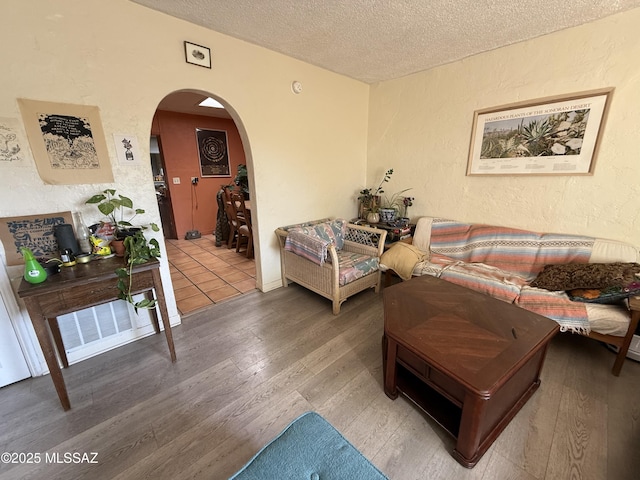living room featuring visible vents, a textured ceiling, wood finished floors, arched walkways, and a textured wall