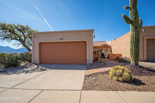 pueblo-style house with stucco siding, a mountain view, concrete driveway, an attached garage, and a tiled roof