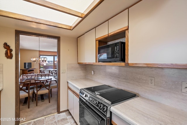 kitchen with an inviting chandelier, black appliances, stone finish floor, light countertops, and backsplash