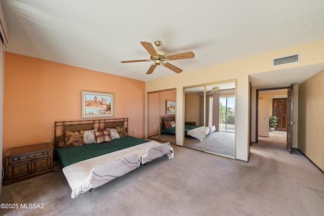 bedroom with visible vents, multiple closets, carpet floors, a textured ceiling, and a ceiling fan