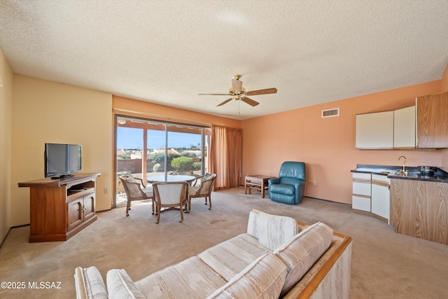 living room with visible vents, light colored carpet, a textured ceiling, and a ceiling fan