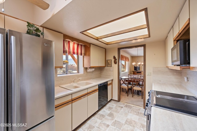 kitchen with a sink, backsplash, stainless steel appliances, an inviting chandelier, and light countertops