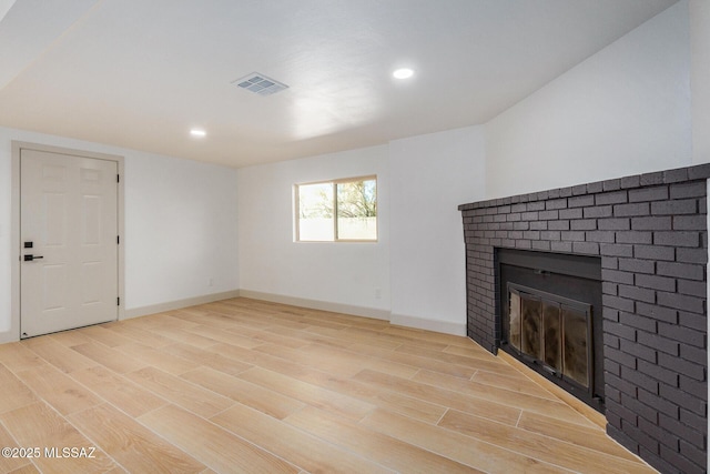 unfurnished living room with visible vents, baseboards, a brick fireplace, and light wood finished floors