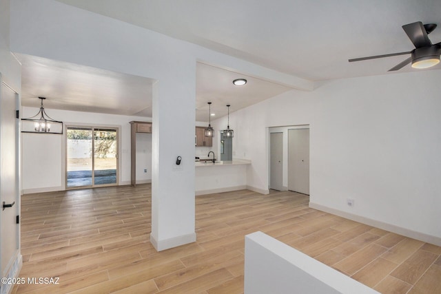unfurnished living room featuring wood tiled floor, ceiling fan with notable chandelier, a sink, baseboards, and vaulted ceiling with beams