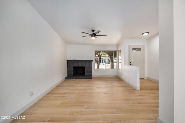 unfurnished living room with a fireplace, a ceiling fan, light wood-style floors, and baseboards