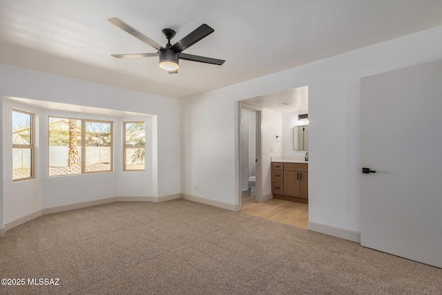 unfurnished bedroom with a ceiling fan, baseboards, ensuite bathroom, and light carpet