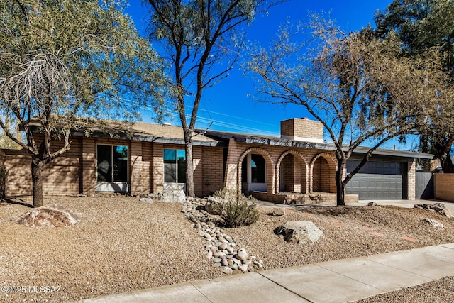 view of front of home featuring brick siding, an attached garage, concrete driveway, and a chimney