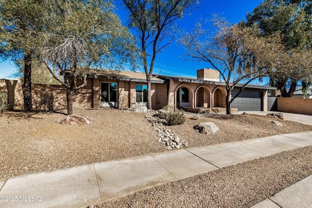 view of front facade featuring concrete driveway, an attached garage, fence, and a chimney