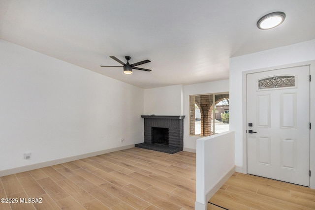 foyer with light wood-type flooring, baseboards, a brick fireplace, and a ceiling fan