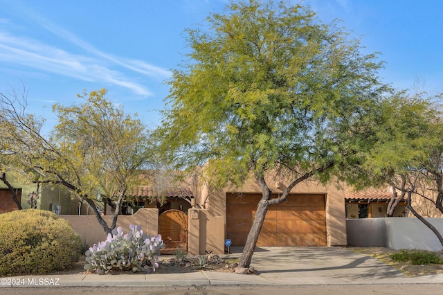 adobe home featuring an attached garage, a fenced front yard, concrete driveway, and a gate