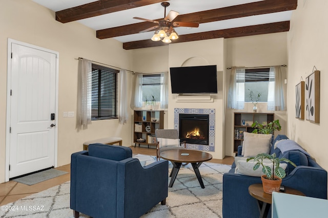 living area featuring a tiled fireplace, a ceiling fan, light tile patterned floors, and beamed ceiling
