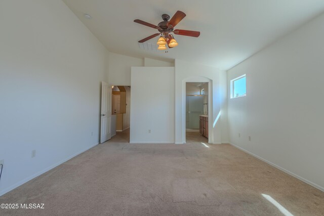 unfurnished bedroom featuring arched walkways, baseboards, lofted ceiling, and light colored carpet