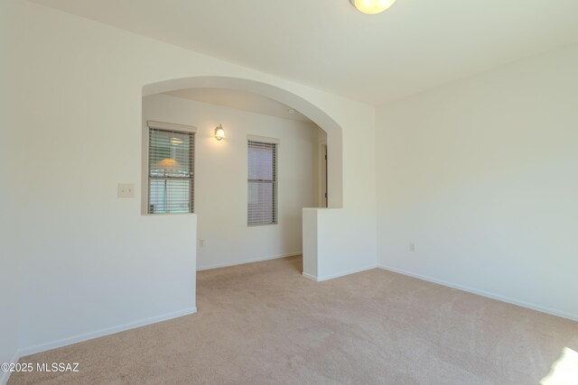 spare room with arched walkways, baseboards, and light carpet