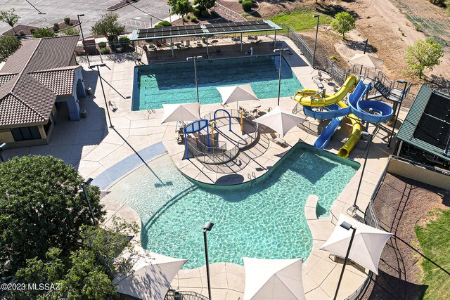 community pool with fence, a water slide, and a patio area