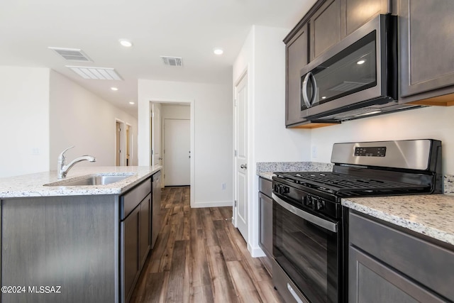kitchen featuring a sink, light stone countertops, appliances with stainless steel finishes, visible vents, and dark wood-style flooring