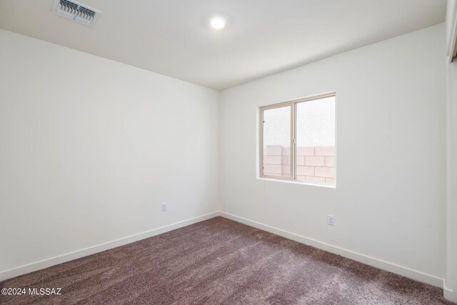 empty room featuring baseboards, visible vents, and dark colored carpet