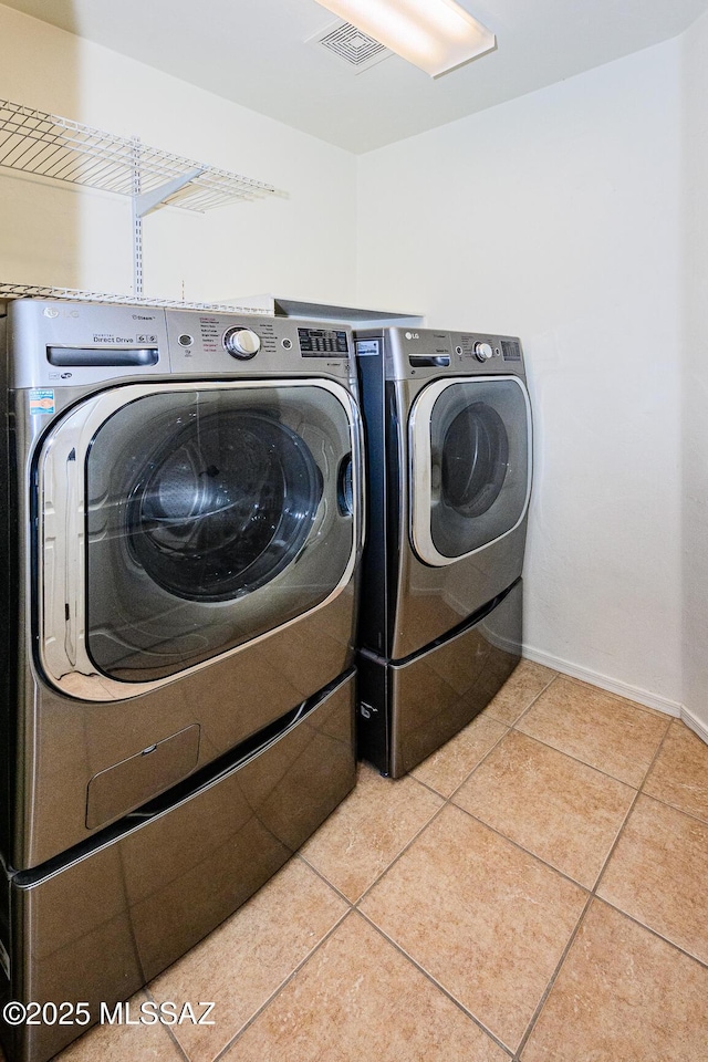 clothes washing area with visible vents, washer and dryer, tile patterned flooring, baseboards, and laundry area
