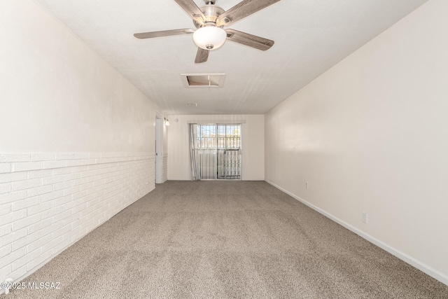 carpeted spare room featuring visible vents, brick wall, attic access, and ceiling fan