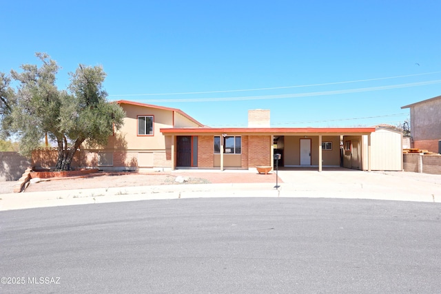 view of front of property with brick siding, an attached carport, fence, a chimney, and driveway