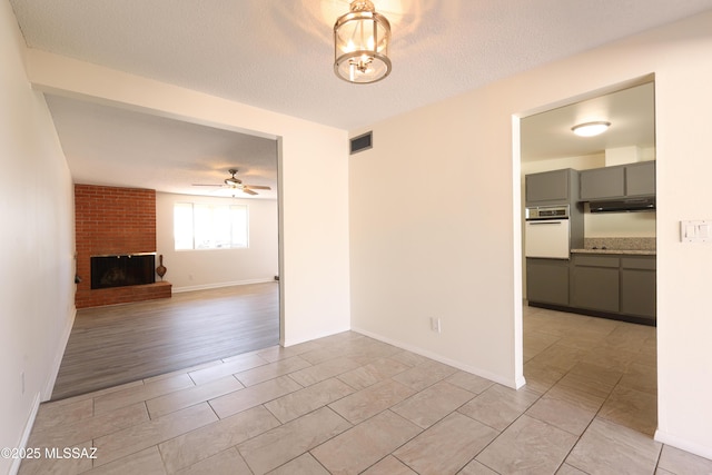 unfurnished living room with a ceiling fan, baseboards, visible vents, a textured ceiling, and a brick fireplace