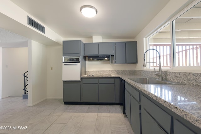 kitchen featuring visible vents, gray cabinetry, oven, under cabinet range hood, and a sink