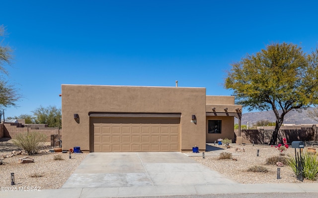pueblo-style house with stucco siding, driveway, an attached garage, and fence