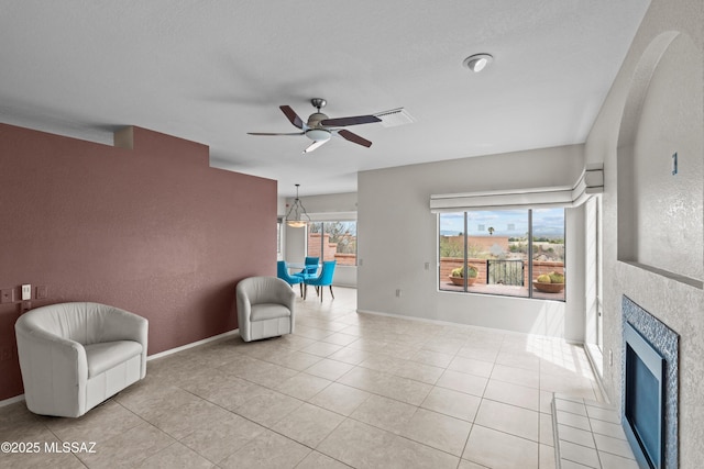 living area with light tile patterned flooring, ceiling fan, a tiled fireplace, and visible vents