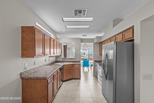 kitchen featuring dark countertops, visible vents, brown cabinetry, appliances with stainless steel finishes, and a sink