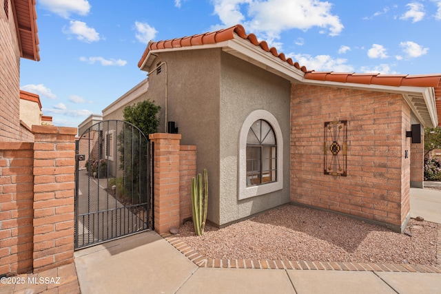 view of side of property with stucco siding, fence, a tile roof, and a gate