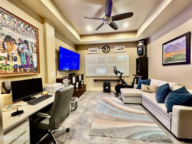 home office with a ceiling fan and a tray ceiling