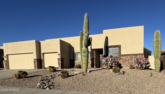 pueblo revival-style home featuring driveway, stone siding, a garage, and stucco siding