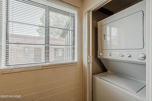 laundry room featuring laundry area, stacked washer and clothes dryer, and concrete block wall