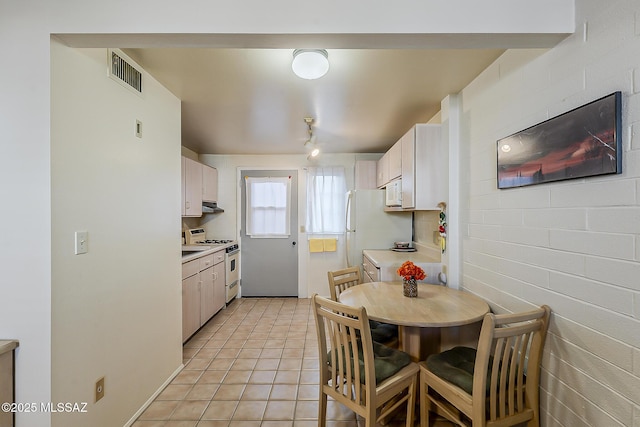 kitchen with white appliances, visible vents, light tile patterned flooring, light countertops, and under cabinet range hood