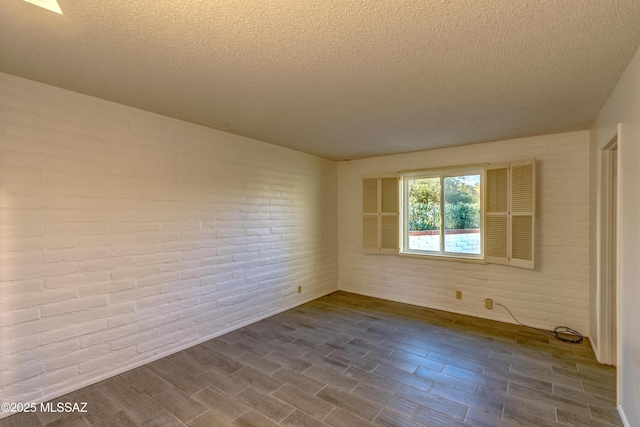 empty room with dark wood-style floors, brick wall, and a textured ceiling