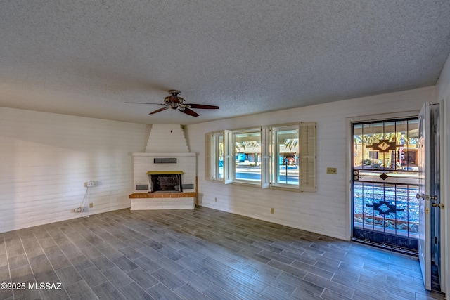 unfurnished living room with wood finish floors, a textured ceiling, a fireplace, and ceiling fan
