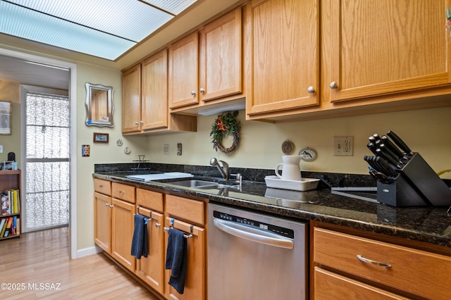 kitchen featuring dark stone countertops, baseboards, a sink, light wood-style floors, and stainless steel dishwasher