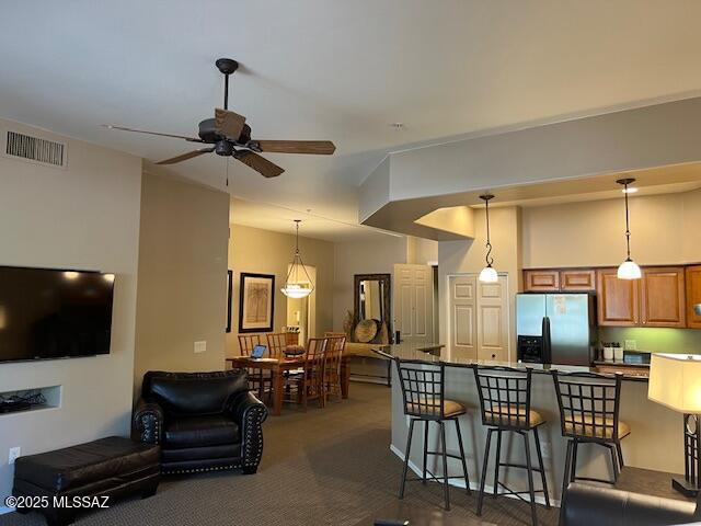 5775 S Camino Del Sol Unit 6104, Green Valley, AZ 85622 - kitchen with stainless steel fridge, brown cabinetry, a kitchen breakfast bar, a ceiling fan, and dark colored carpet