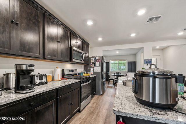 34932 S Iron Jaw Dr, Red Rock, AZ 85145 - kitchen featuring visible vents, light wood-style flooring, light stone counters, appliances with stainless steel finishes, and dark brown cabinets